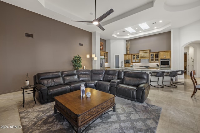 tiled living room featuring ceiling fan, a towering ceiling, sink, and a tray ceiling