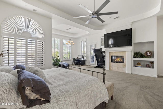 bedroom with ceiling fan with notable chandelier, carpet floors, a tile fireplace, and a tray ceiling