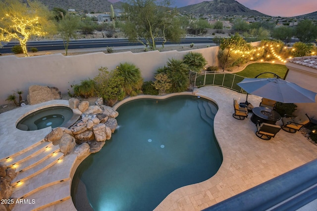 pool at dusk featuring a mountain view, a patio, and an in ground hot tub