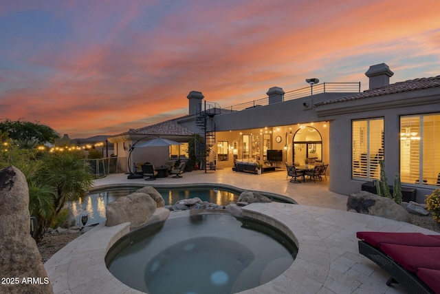 pool at dusk with an in ground hot tub, a patio, and an outdoor living space