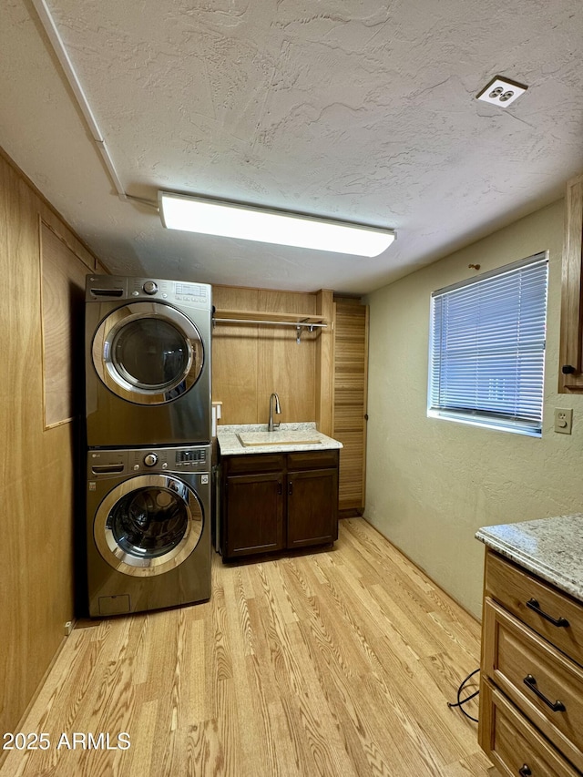 laundry area featuring stacked washer and clothes dryer, sink, cabinets, light hardwood / wood-style flooring, and a textured ceiling