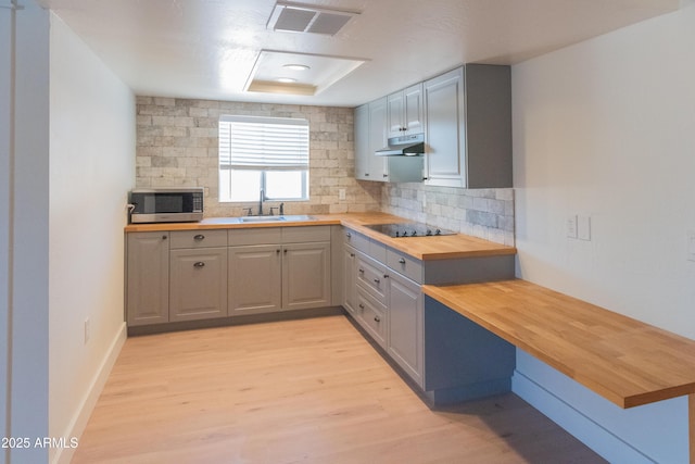 5102 W Whispering Wind Dr, Glendale, AZ 85310 - kitchen featuring butcher block counters, stainless steel microwave, black electric stovetop, under cabinet range hood, and tasteful backsplash