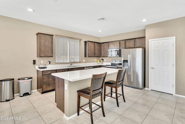 kitchen featuring stainless steel appliances, a breakfast bar, a kitchen island, dark brown cabinets, and light tile patterned flooring