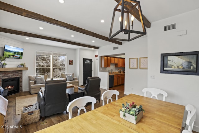 dining space with beamed ceiling, dark wood-style flooring, a brick fireplace, and visible vents