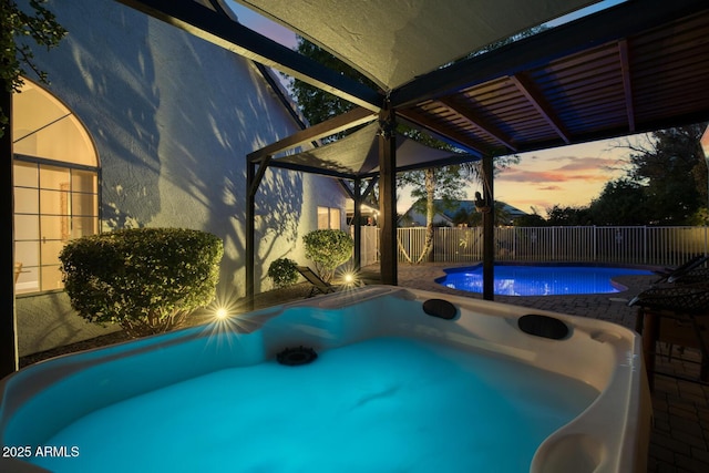 pool at dusk featuring a hot tub