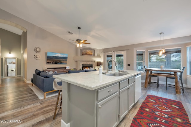 kitchen with hardwood / wood-style floors, lofted ceiling, sink, stainless steel dishwasher, and a center island with sink