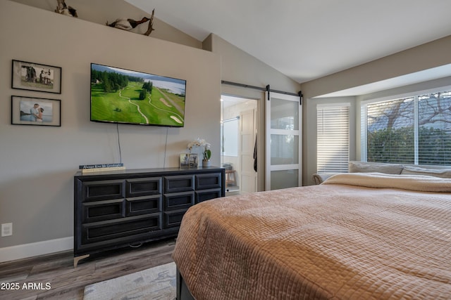 bedroom with hardwood / wood-style flooring, a barn door, and vaulted ceiling