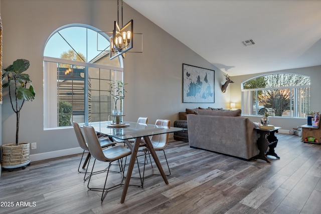 dining room with hardwood / wood-style flooring, high vaulted ceiling, and an inviting chandelier