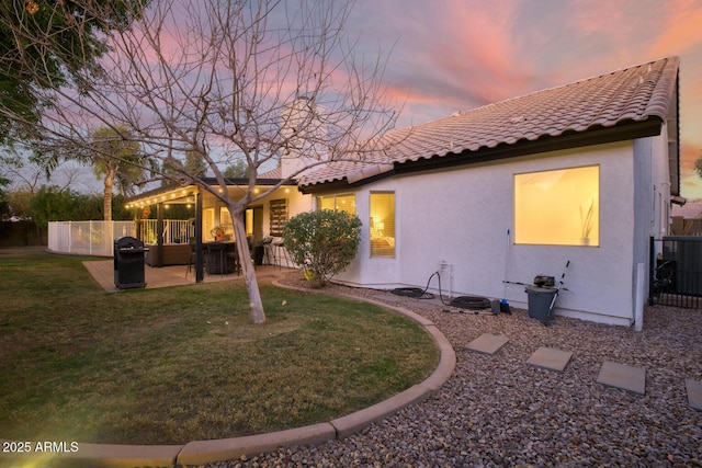 back house at dusk featuring a yard, a patio, and central air condition unit