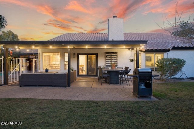 back house at dusk with a patio, outdoor lounge area, and a lawn