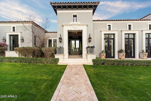 entrance to property with stucco siding, a tiled roof, a lawn, and french doors