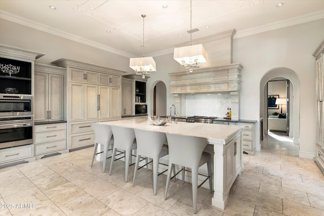 kitchen featuring arched walkways, a kitchen island with sink, tasteful backsplash, a kitchen bar, and crown molding