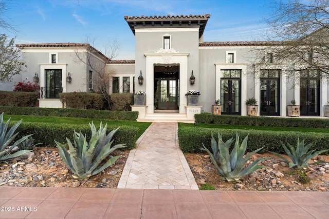 view of exterior entry with french doors, a tile roof, and stucco siding