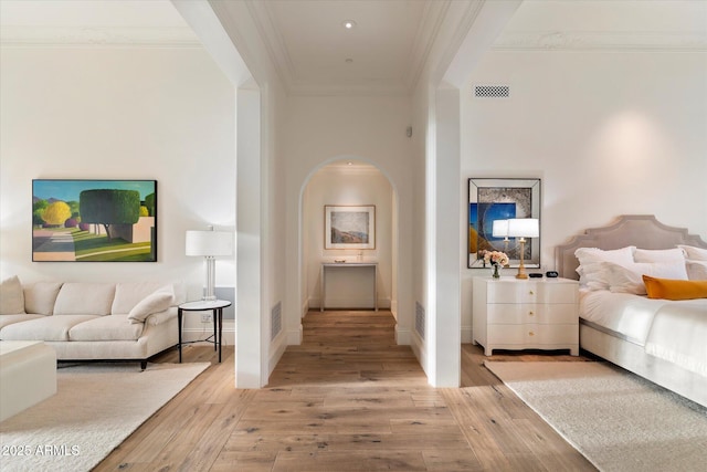 bedroom featuring arched walkways, light wood-style flooring, ornamental molding, and visible vents