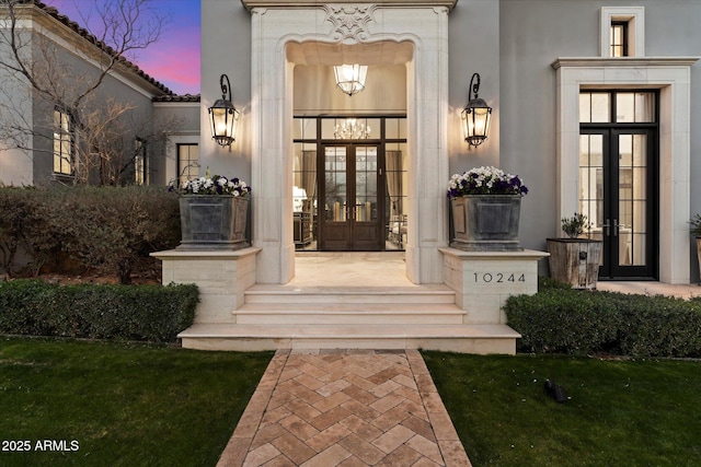 exterior entry at dusk featuring stucco siding and french doors