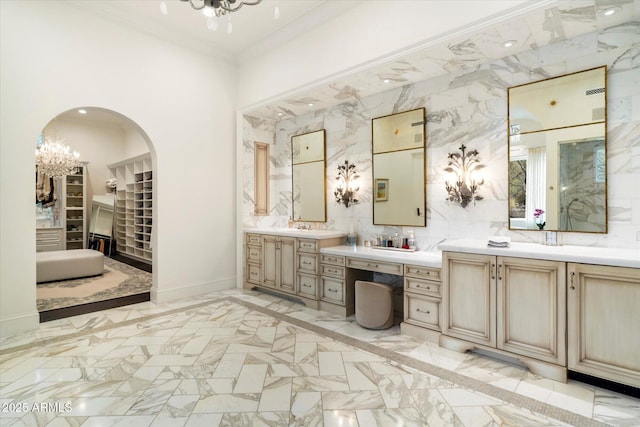 full bathroom featuring marble finish floor, a notable chandelier, crown molding, two vanities, and baseboards