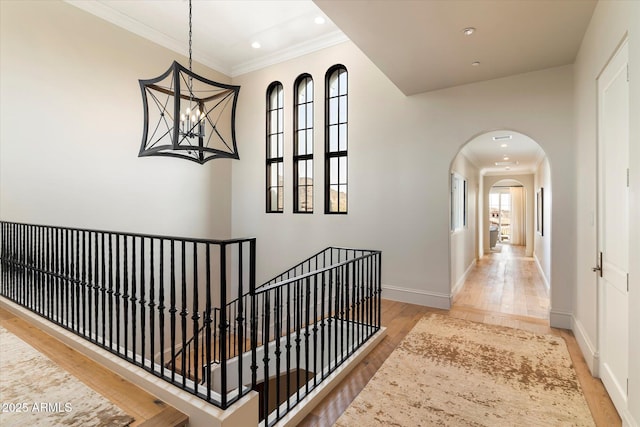 corridor with baseboards, arched walkways, wood finished floors, and ornamental molding