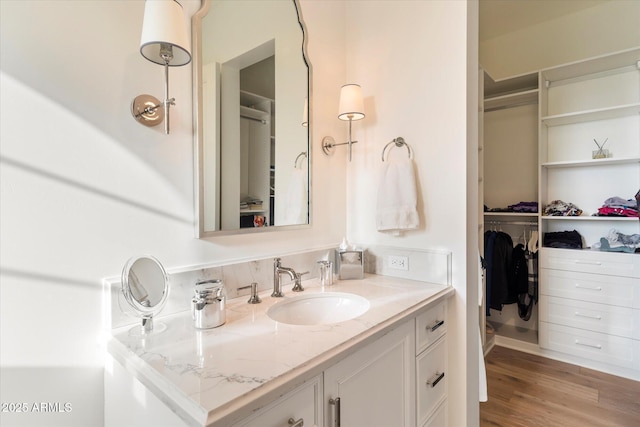 bathroom with a spacious closet, wood finished floors, and vanity