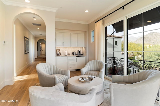 sitting room with a healthy amount of sunlight, light wood-style flooring, arched walkways, and baseboards