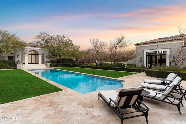 pool at dusk with a yard, french doors, an exterior structure, and a patio