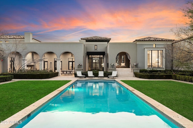 rear view of house featuring stucco siding, a patio, and a yard