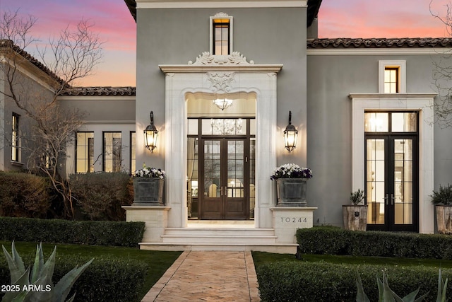 view of exterior entry with french doors, a tile roof, and stucco siding