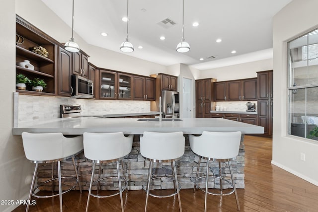 kitchen featuring dark wood-type flooring, a breakfast bar, dark brown cabinets, stainless steel appliances, and decorative light fixtures