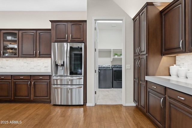 kitchen featuring decorative backsplash, washing machine and dryer, dark brown cabinetry, stainless steel refrigerator with ice dispenser, and light hardwood / wood-style flooring