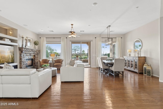 living room with ceiling fan with notable chandelier, a fireplace, and dark hardwood / wood-style flooring