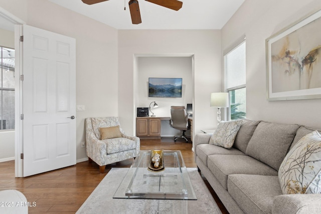 living room with dark wood-type flooring, ceiling fan, and built in desk