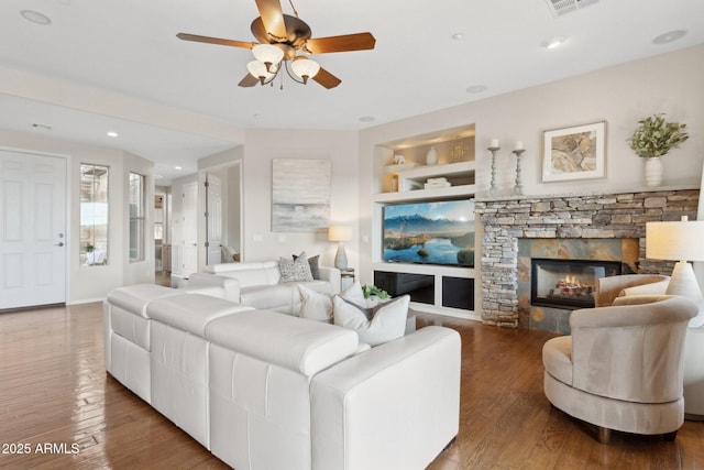 living room featuring hardwood / wood-style flooring, ceiling fan, a stone fireplace, and built in shelves