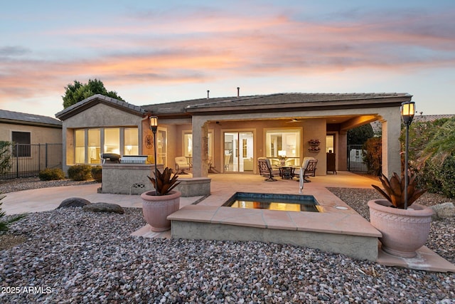 back house at dusk with an outdoor kitchen, a pool with hot tub, ceiling fan, and a patio area