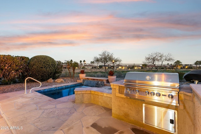 pool at dusk featuring pool water feature, an outdoor kitchen, grilling area, and a patio area