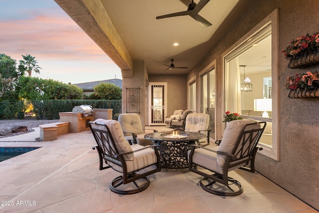 patio terrace at dusk with an outdoor kitchen, ceiling fan, and an outdoor fire pit