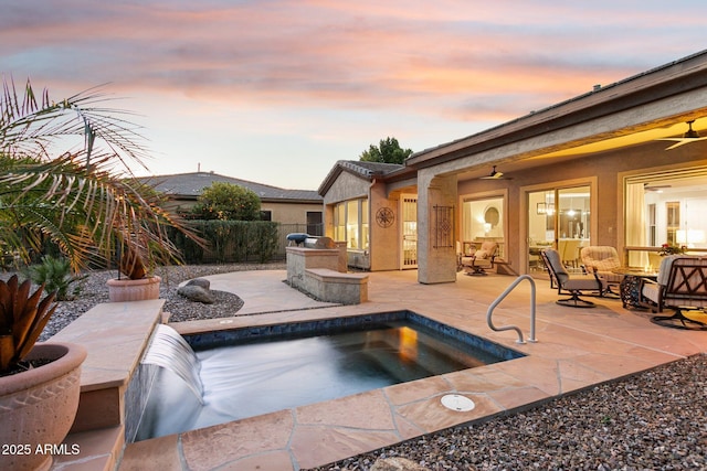 pool at dusk with a hot tub, a patio, an outdoor kitchen, and ceiling fan