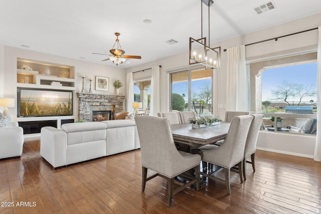 dining area featuring hardwood / wood-style flooring, ceiling fan, a stone fireplace, and built in features