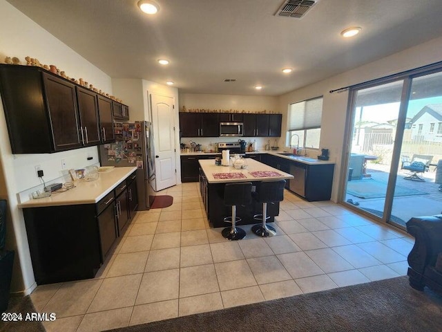 kitchen featuring dark brown cabinets, a center island, light tile patterned flooring, and appliances with stainless steel finishes