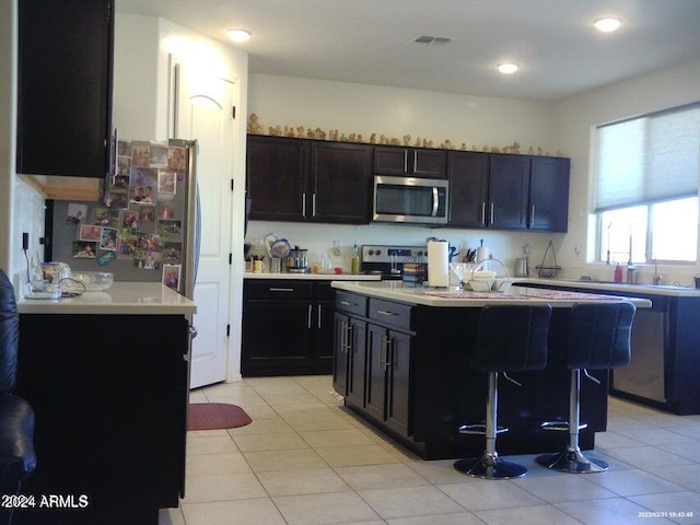 kitchen with a breakfast bar, a center island, light tile patterned flooring, and dark brown cabinets