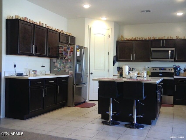 kitchen with a center island, a kitchen breakfast bar, dark brown cabinets, light tile patterned flooring, and stainless steel appliances