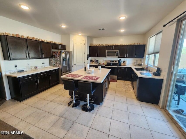 kitchen with a breakfast bar, sink, light tile patterned floors, a kitchen island, and stainless steel appliances