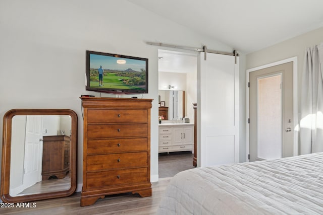 bedroom featuring a barn door, vaulted ceiling, connected bathroom, and light hardwood / wood-style flooring