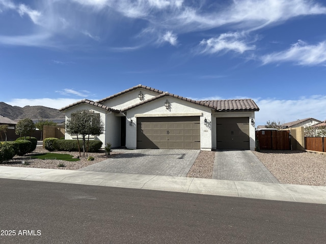 view of front facade featuring a tiled roof, an attached garage, decorative driveway, and a gate