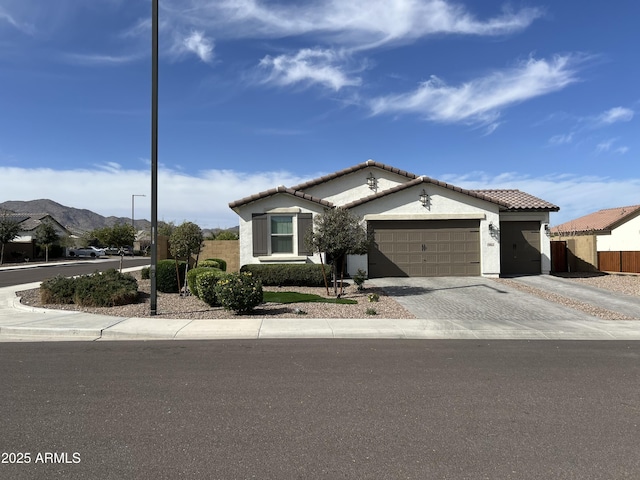 view of front of home featuring decorative driveway, fence, a mountain view, a garage, and a tiled roof