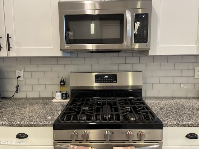 kitchen featuring white cabinets, appliances with stainless steel finishes, decorative backsplash, and dark stone countertops