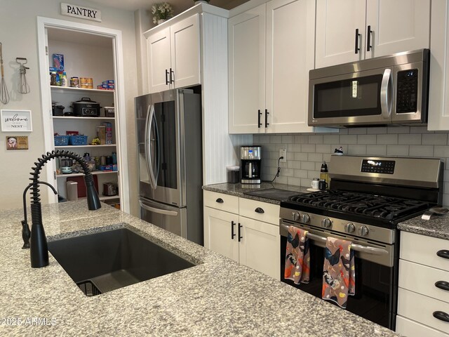 kitchen featuring decorative backsplash, light stone countertops, white cabinets, a sink, and appliances with stainless steel finishes