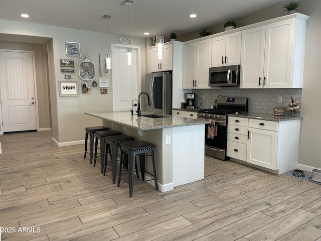 kitchen with appliances with stainless steel finishes, a breakfast bar, light wood-style floors, baseboards, and decorative backsplash