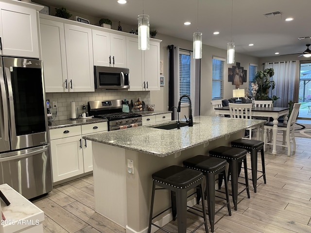 kitchen featuring visible vents, a sink, decorative backsplash, stainless steel appliances, and light wood-type flooring