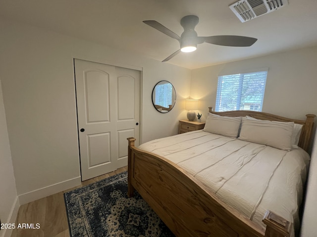 bedroom featuring ceiling fan, wood finished floors, visible vents, baseboards, and a closet