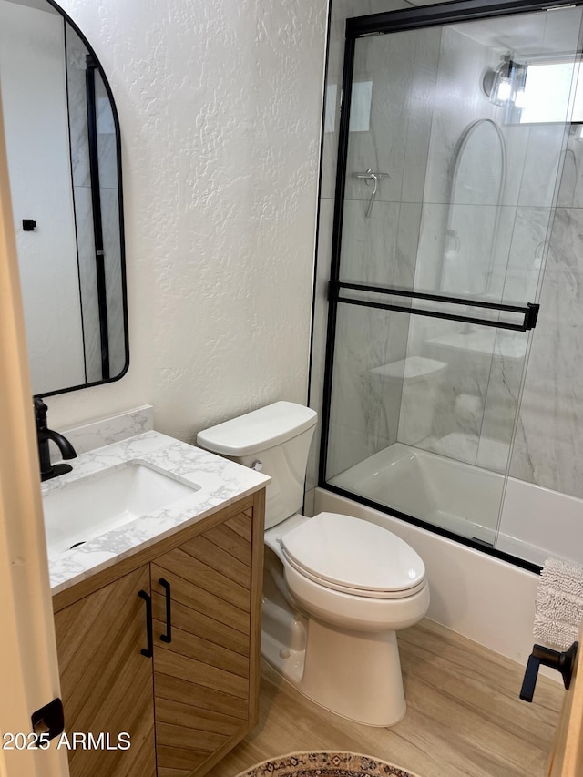 bathroom with toilet, bath / shower combo with glass door, wood finished floors, and a textured wall