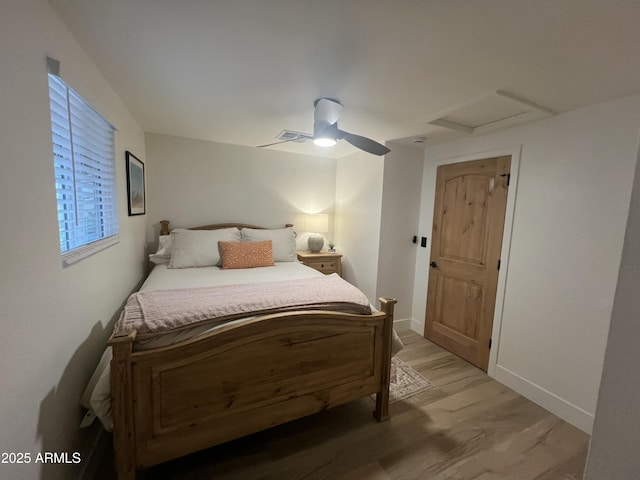 bedroom with light wood finished floors, visible vents, attic access, a ceiling fan, and baseboards